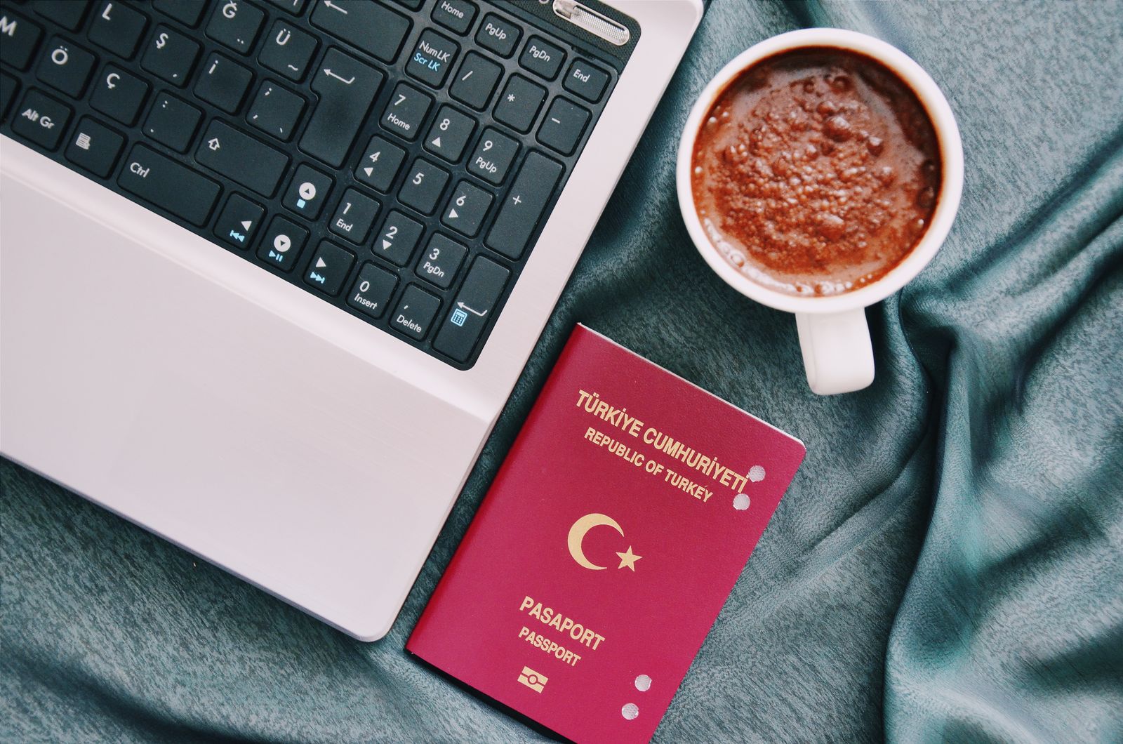 Photo: Gül Işık / Pexels A red Republic of Türkiye passport beside a laptop and a cup of Turkish coffee, the end result of a citizenship-by-investment file